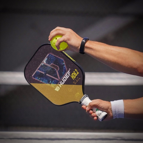 hand holding a pickleball paddle about to hit a ball